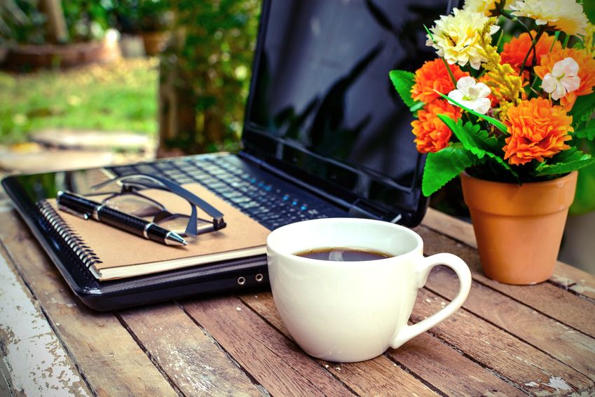 cup of coffee and laptop on wooden table with flower and notebook in the garden, Vintage style